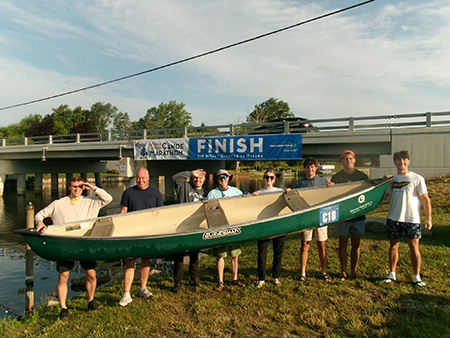 M4 Marina Cox and other team members hold up their canoe at finish line of the Consumers Energy AuSable River Challenge 120